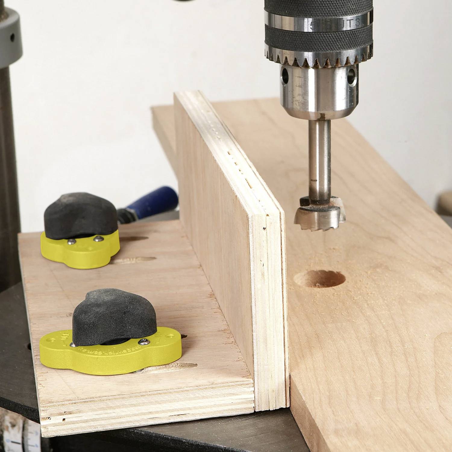 Wiertarka stołowa wierci otwór w kawałku drewna mocno zaciśniętym na stole warsztatowym, obrazując proces obróbki drewna.