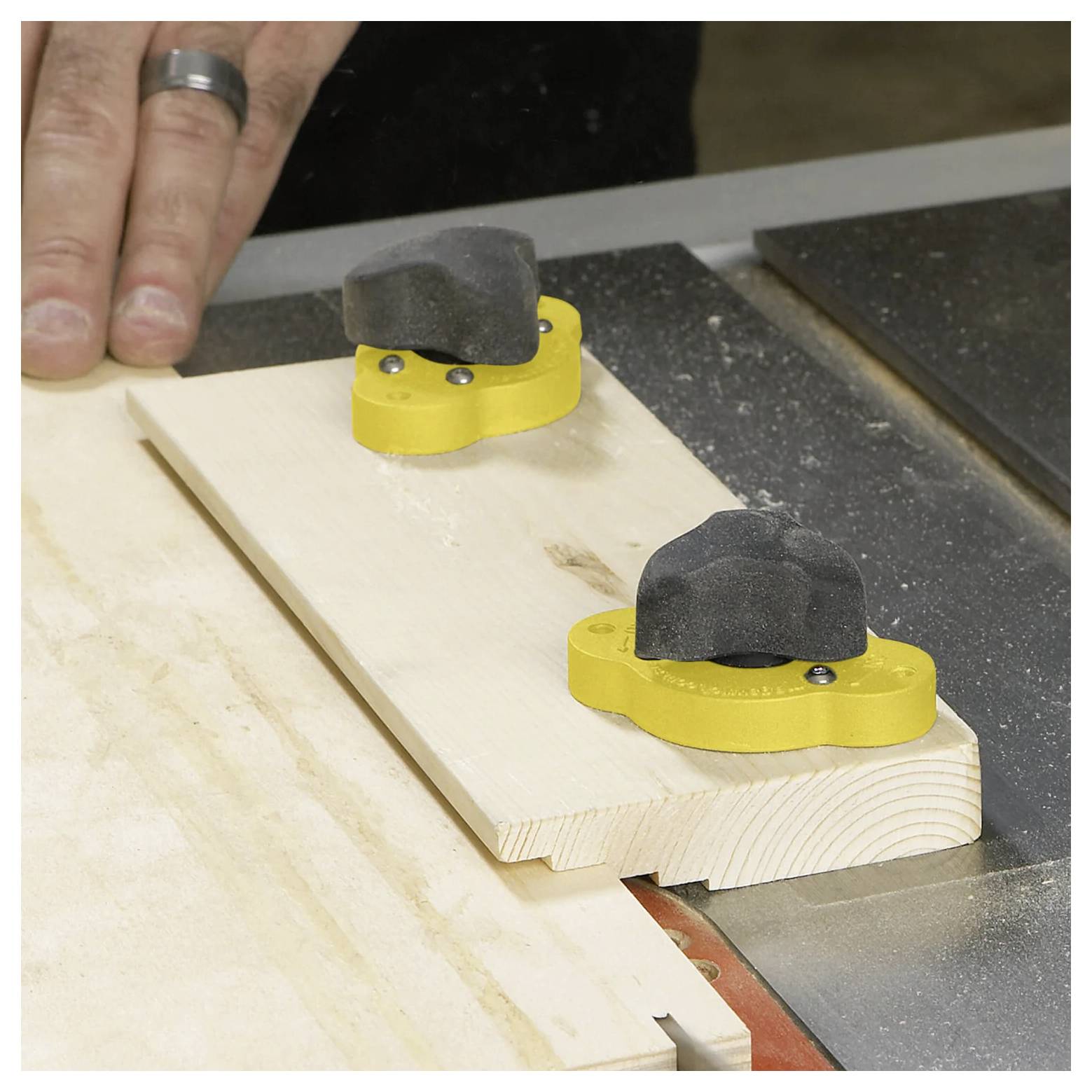 Przyrząd stolarski z żółtą podstawą mocno trzyma drewnianą deskę, podczas gdy ręka przygotowuje się do wykonania precyzyjnych cięć piłą stołową.