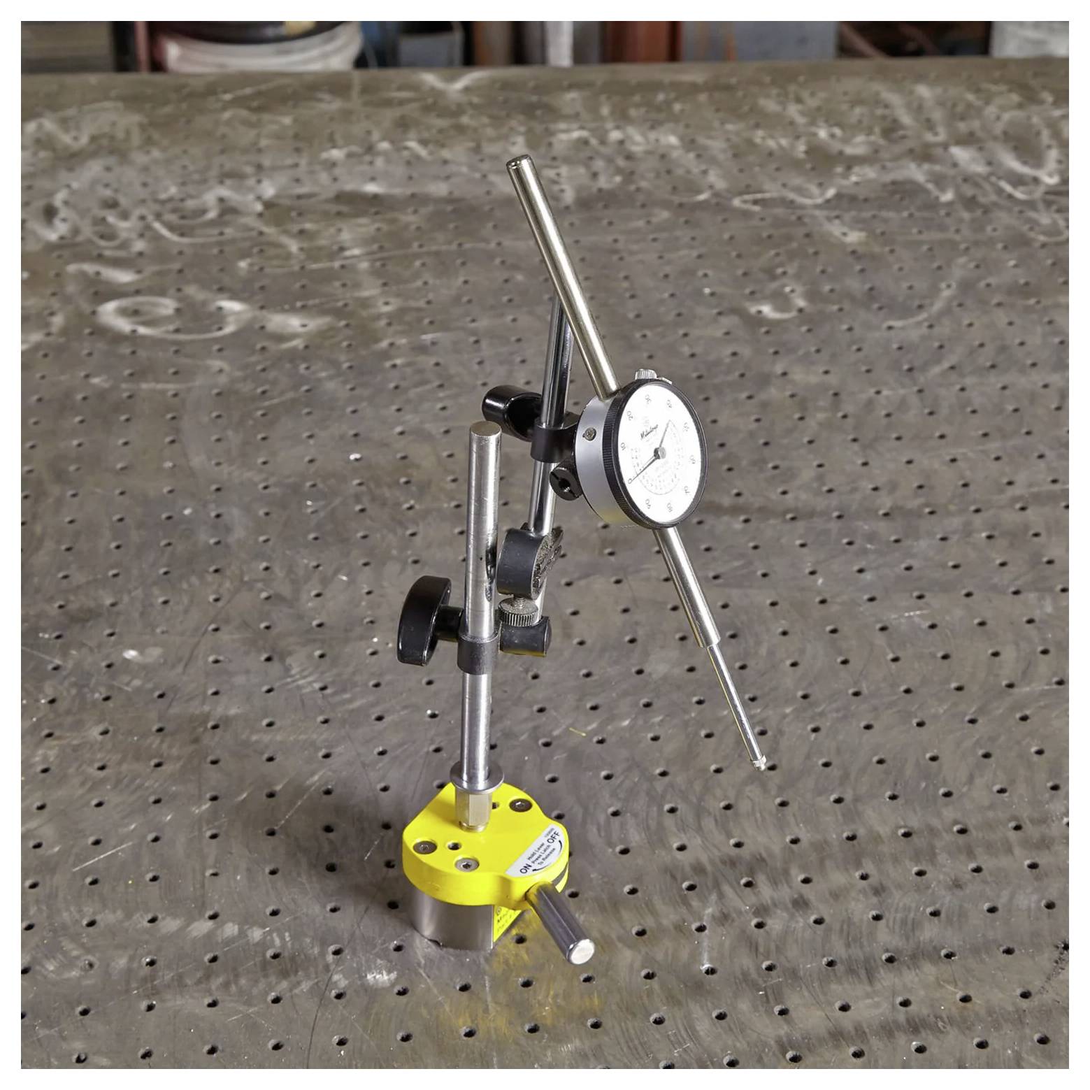 Wskaźnik zegarowy zamocowany na podstawie magnetycznej jest umieszczony na perforowanym stole metalowym, używany do precyzyjnych pomiarów i wyrównywania w zadaniach inżynieryjnych.