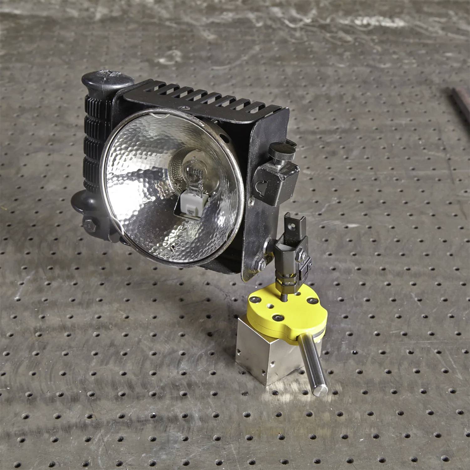 Metalowy stół warsztatowy wyposażony jest w przemysłową lampę, umieszczoną obok uchwytu na narzędzia z sześciokątną żółtą podstawą, prezentujący precyzyjne narzędzia.