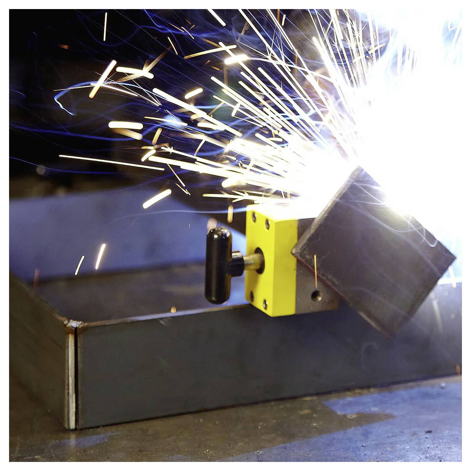 Jasna iskra spawalnicza przelatuje między dwoma kawałkami metalu łączonymi w warsztacie, podkreślając intensywność spawania.