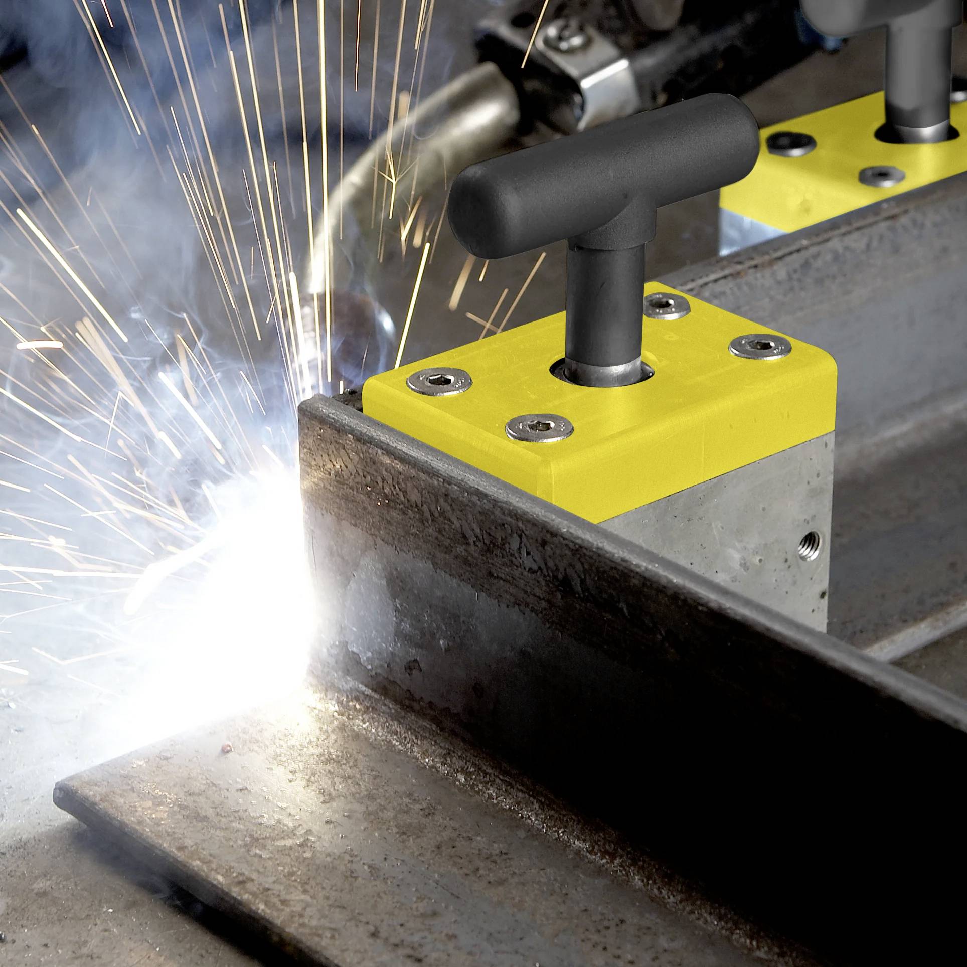 Zbliżenie spawacza używającego zacisku magnetycznego do przytrzymania elementów metalowych, z jasnymi iskrami lecącymi w momencie przyłożenia palnika spawalniczego.