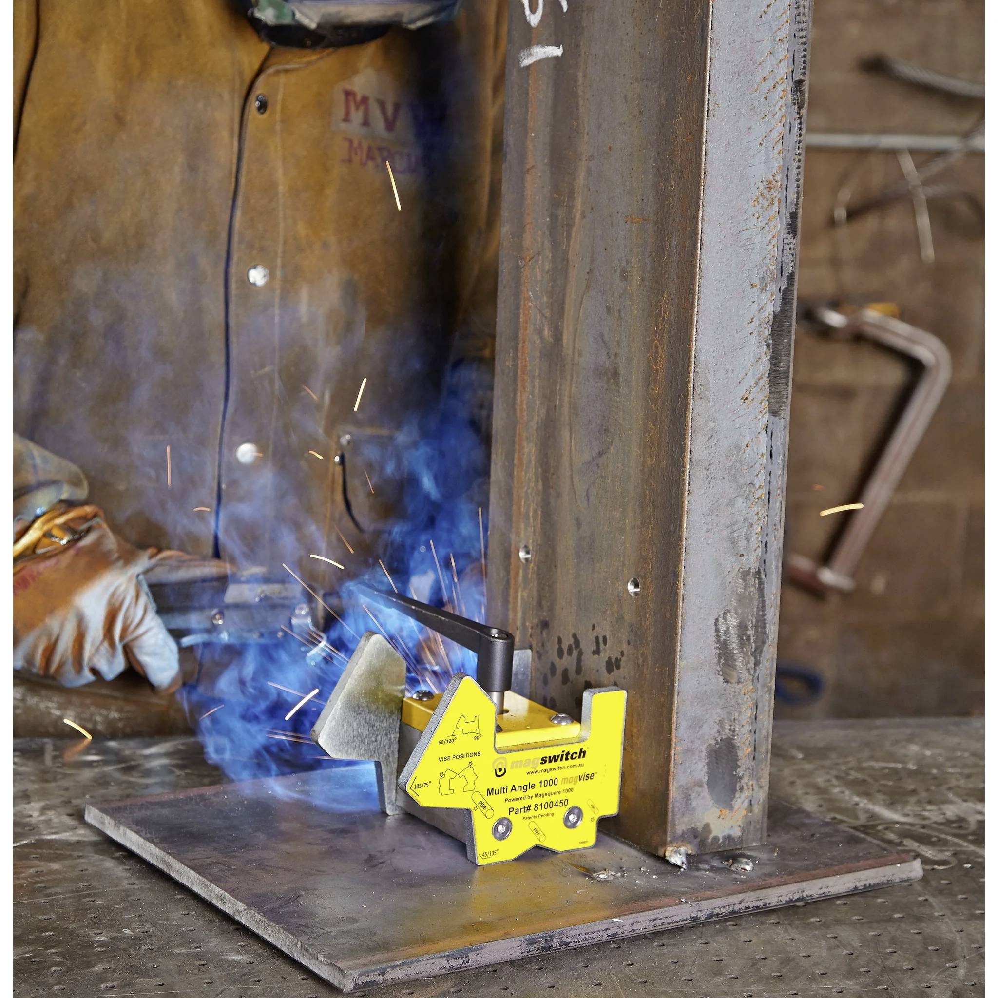 Spawacz w odzieży ochronnej pracuje przy metalowej strukturze. Zacisk magnetyczny oznaczony jako 'Model PMK-200 2000 lbs Pull 181821000' przytrzymuje metal.