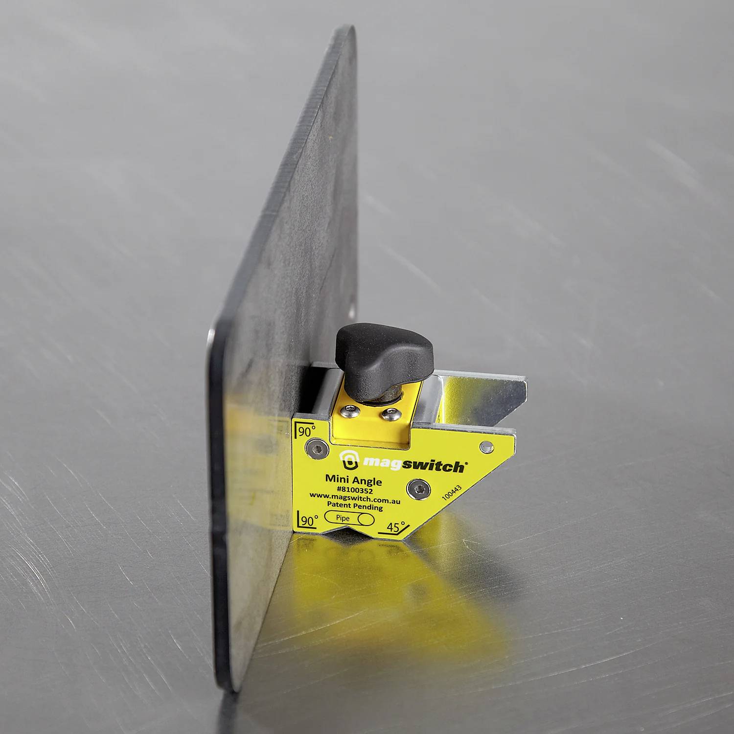 Narzędzie magnetyczne "Mini Angle" przymocowane do powierzchni metalowej, demonstrujące możliwość trzymania materiałów pod precyzyjnymi kątami 45, 90 i 135 stopni.
