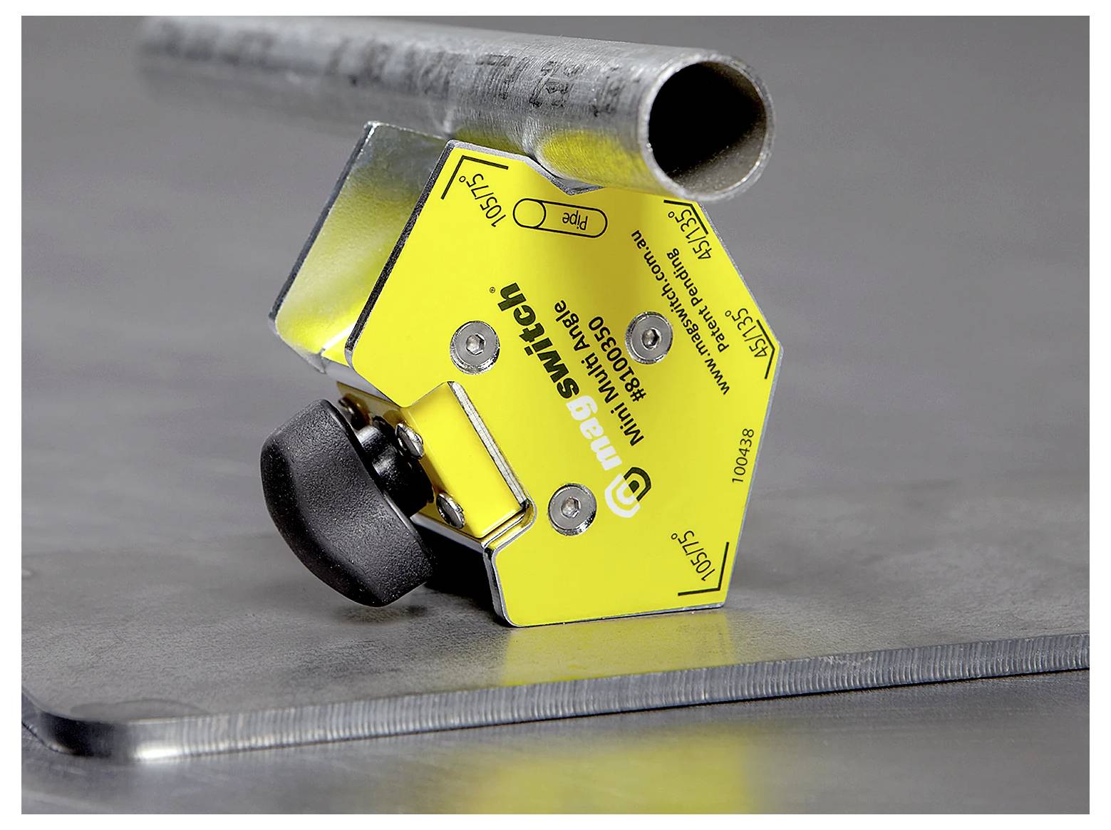 Żółty przełącznik magnetyczny zamontowany na metalowej powierzchni, zabezpieczający cylindryczną metalową rurę nad płaskim arkuszem.