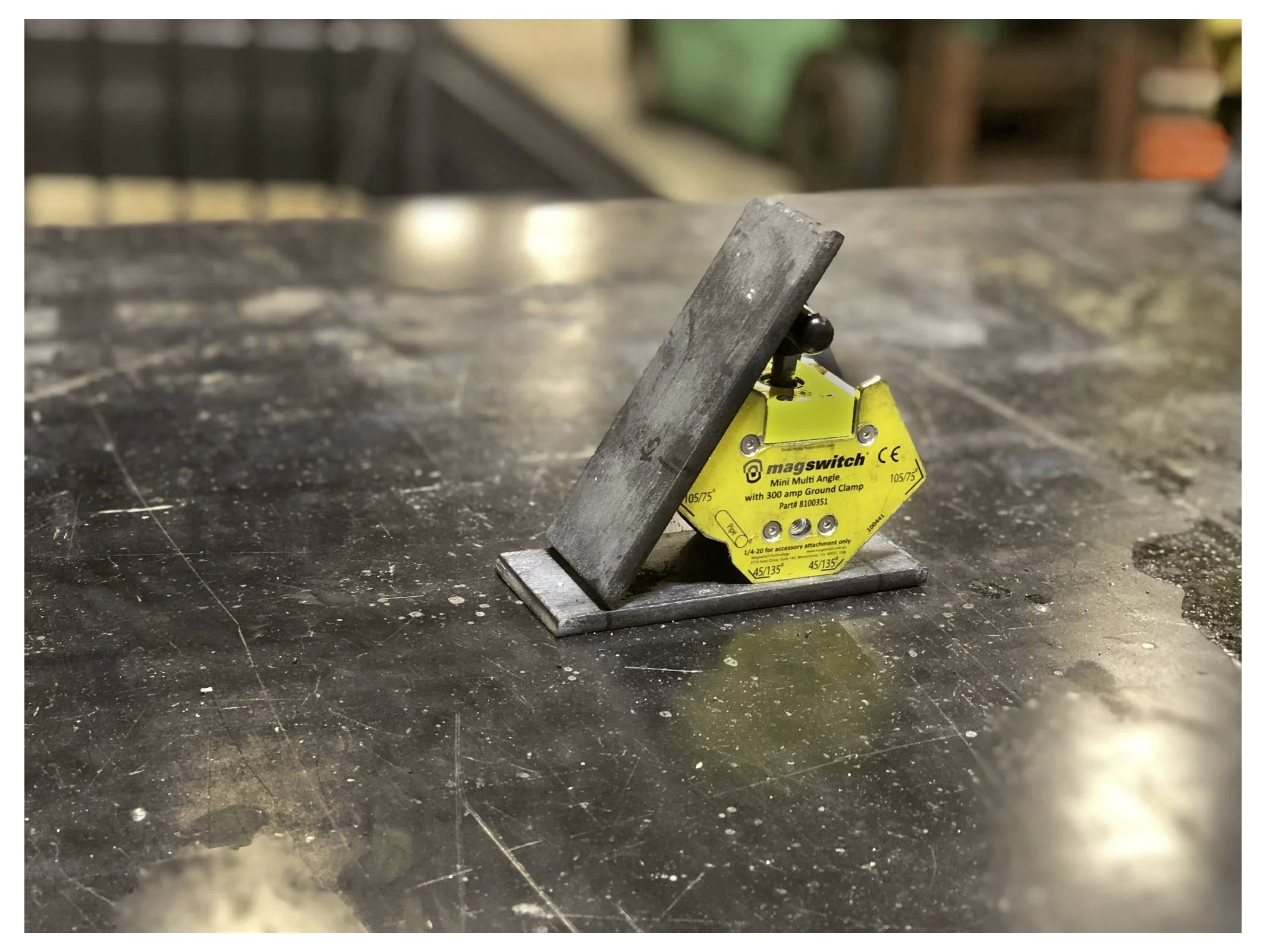 Metalowy obiekt jest trzymany pionowo na stole za pomocą żółtego narzędzia magnetycznego oznaczonego jako 'mag-switch'. Stół posiada ciemną, błyszczącą powierzchnię.