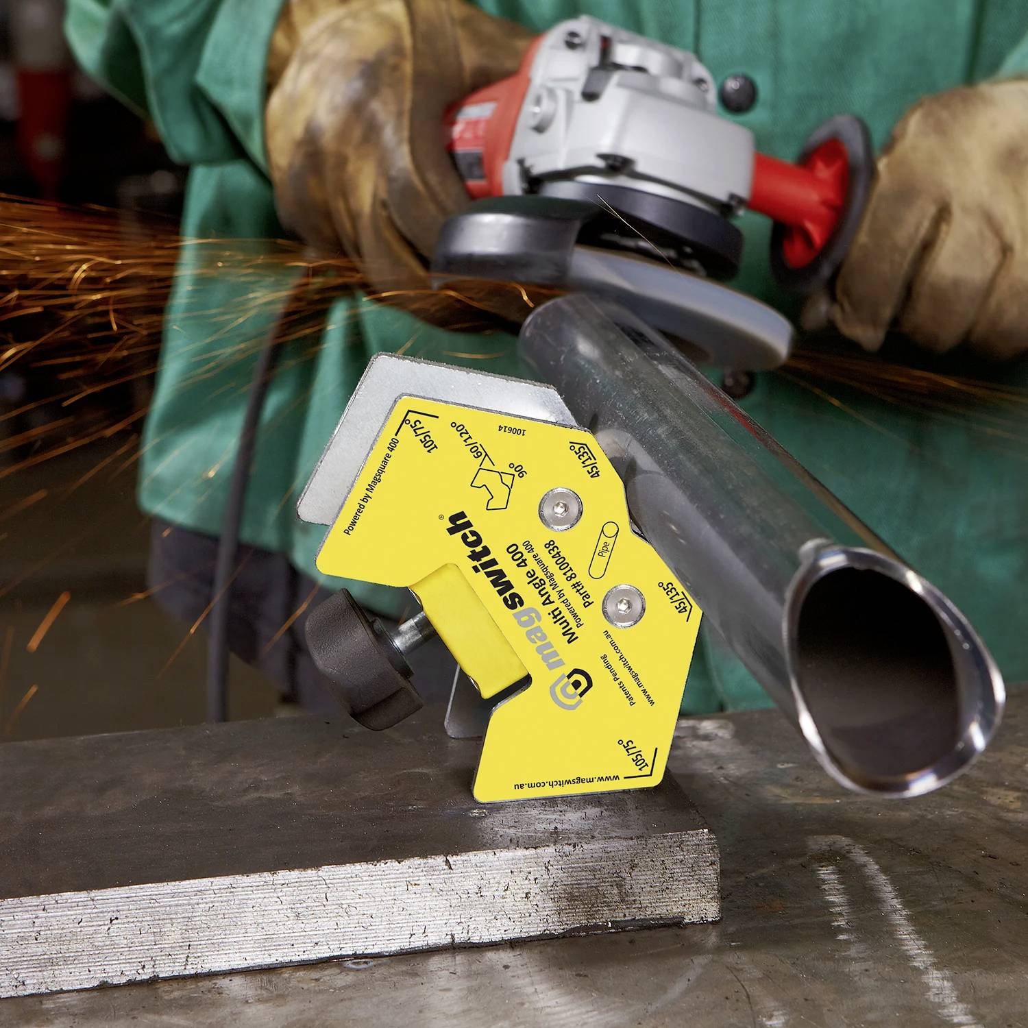 Osoba używa szlifierki kątowej do cięcia metalowej rury, przy czym wokół lecą iskry. W pobliżu znajduje się żółty magnetyczny wspornik oznaczony napisem 'Magswitch Welding'.