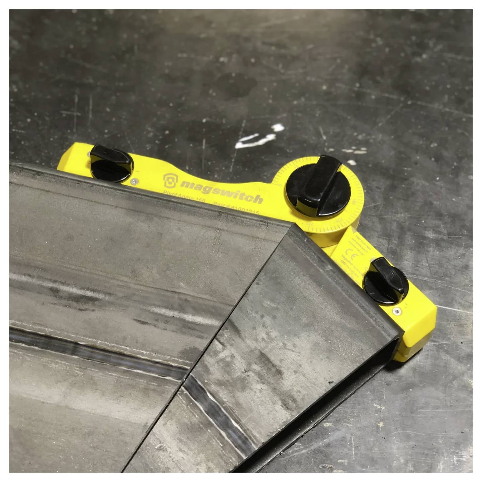 Żółte narzędzie oznaczone etykietą 'magswitch' łączy arkusze metalu pod precyzyjnym kątem na drewnianej powierzchni, sugerując zastosowanie w obróbce metali.