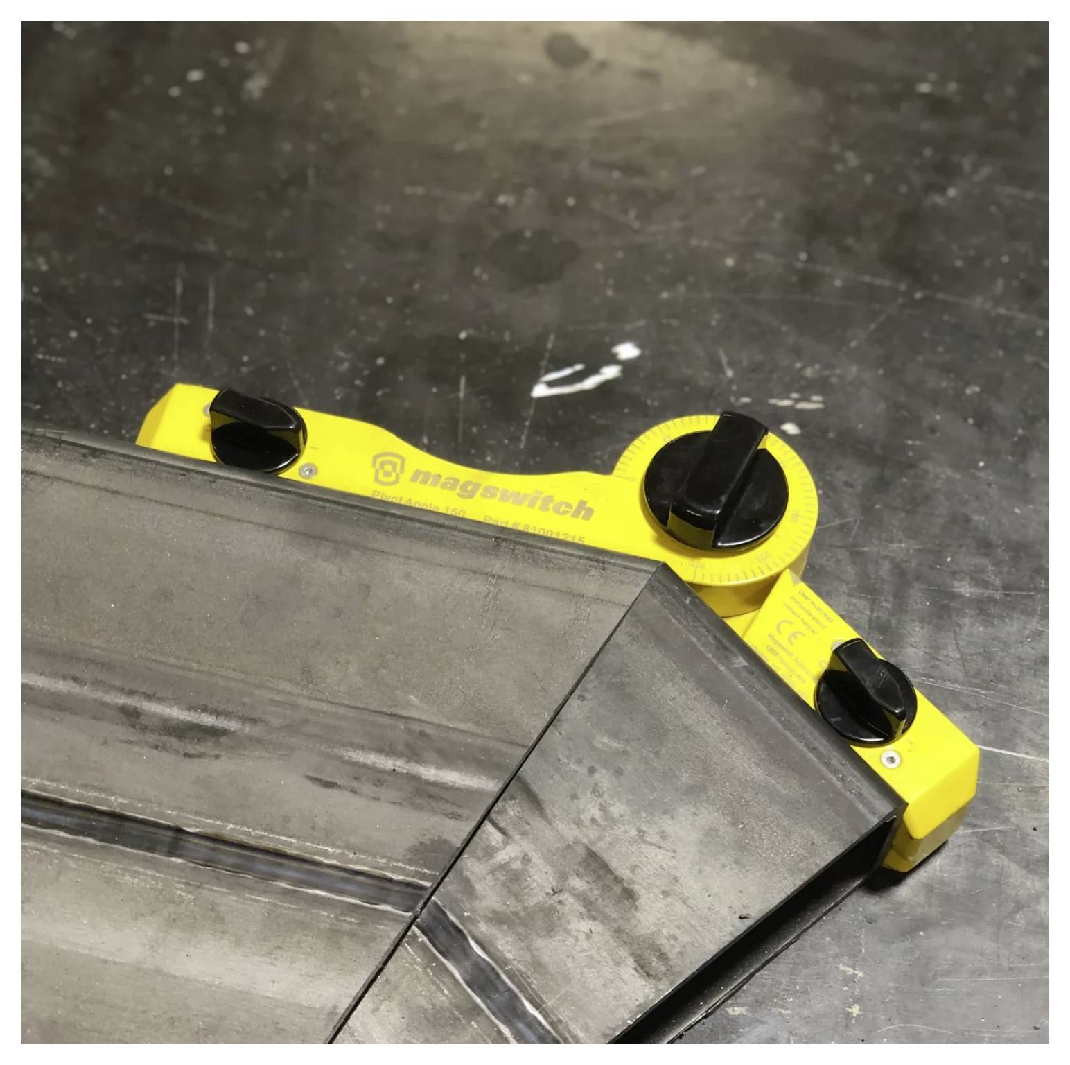 Żółty magnetyczny kątownik spawalniczy mocuje dwie metalowe części pod precyzyjnym kątem na stole warsztatowym.