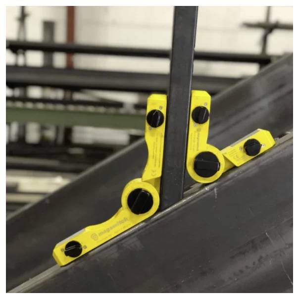 Żółty magnetyczny miernik kąta znajdujący się między dwoma przecinającymi się metalowymi belkami w środowisku przemysłowym.
