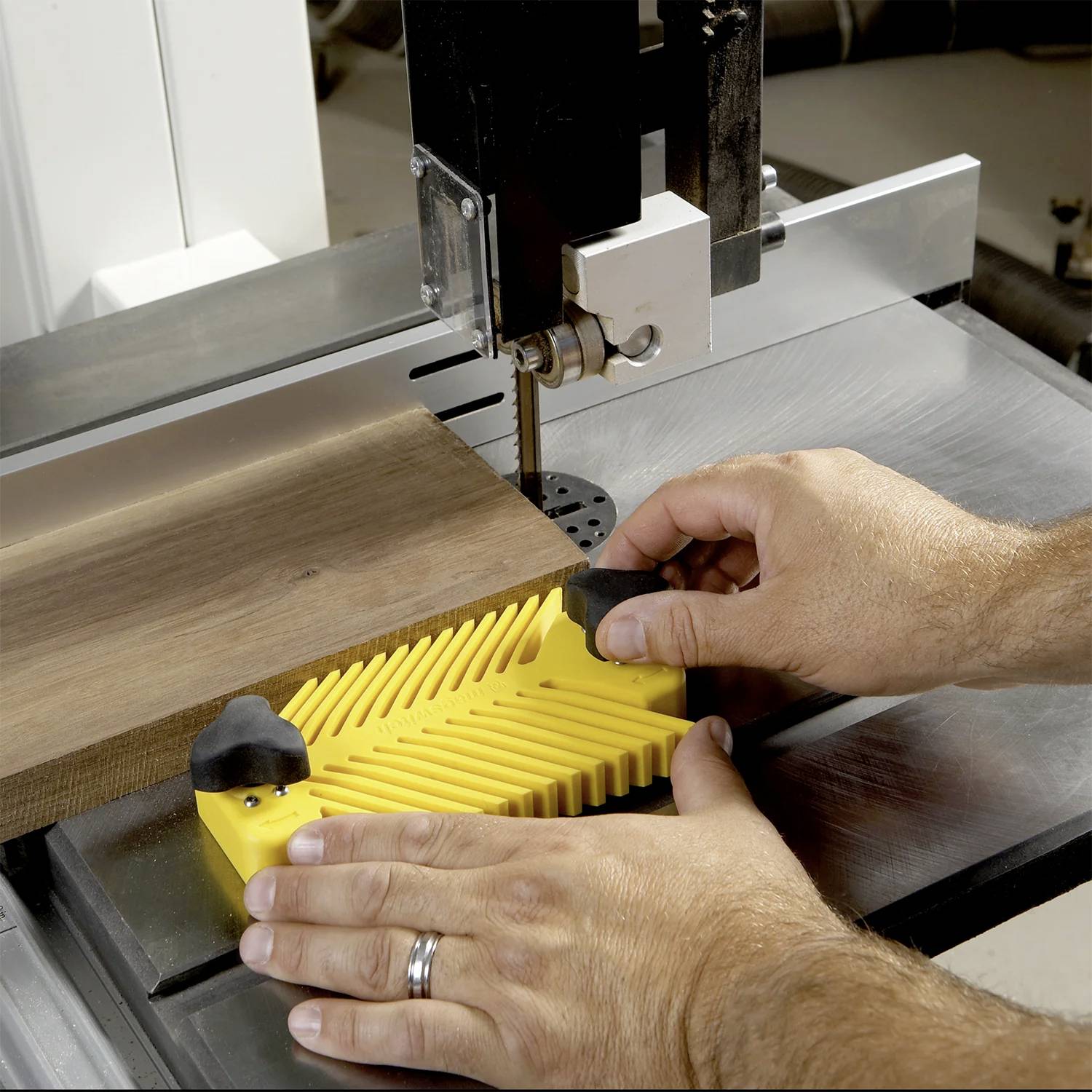 Osoba używa piły stołowej z żółtym popychaczem, aby bezpiecznie prowadzić kawałek drewna, podkreślając bezpieczne praktyki w obróbce drewna.