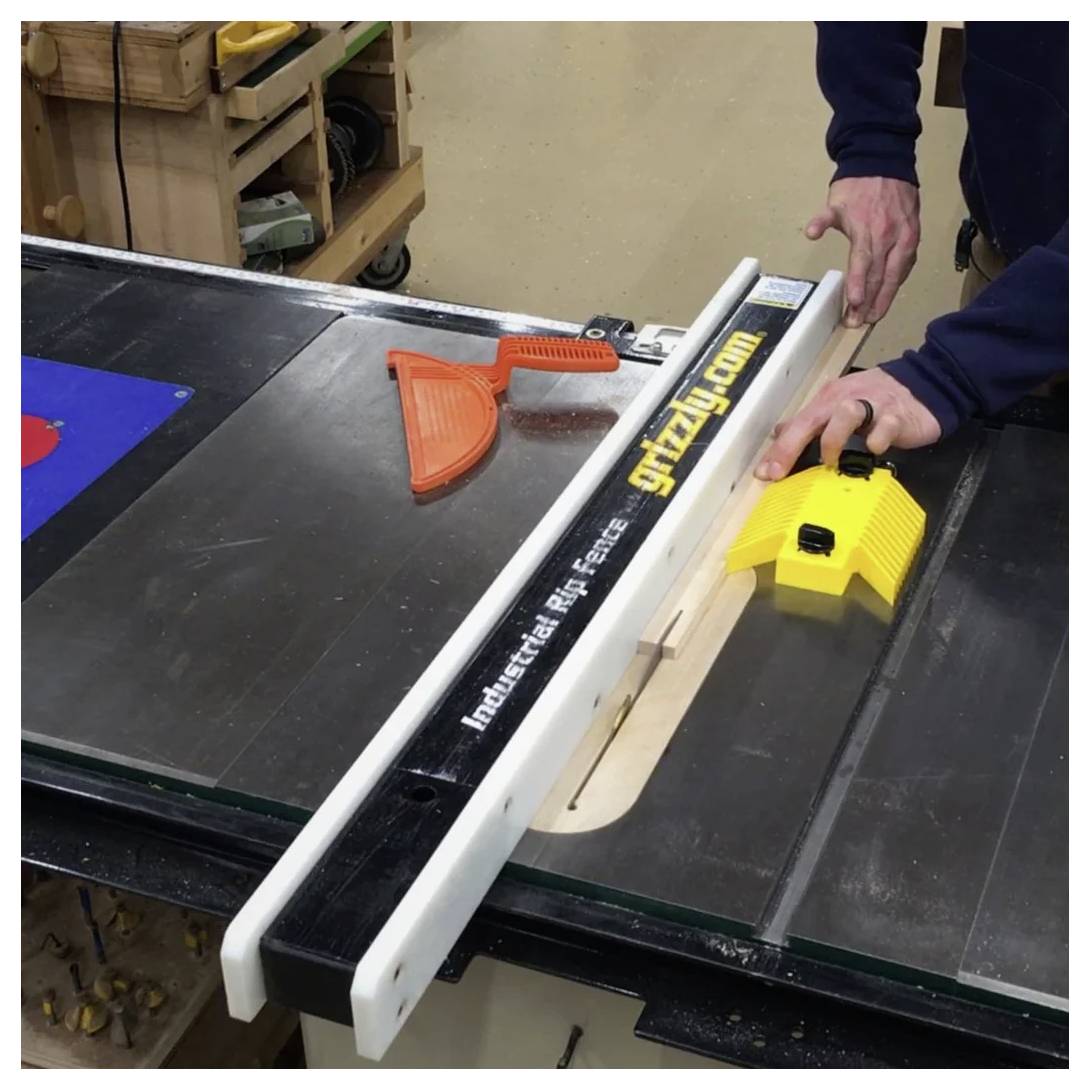 Osoba prowadzi kawałek drewna przez piłę stołową z prowadnicą oznaczoną marką 'grizzly.com', używając żółtego bezpiecznego pchacza.