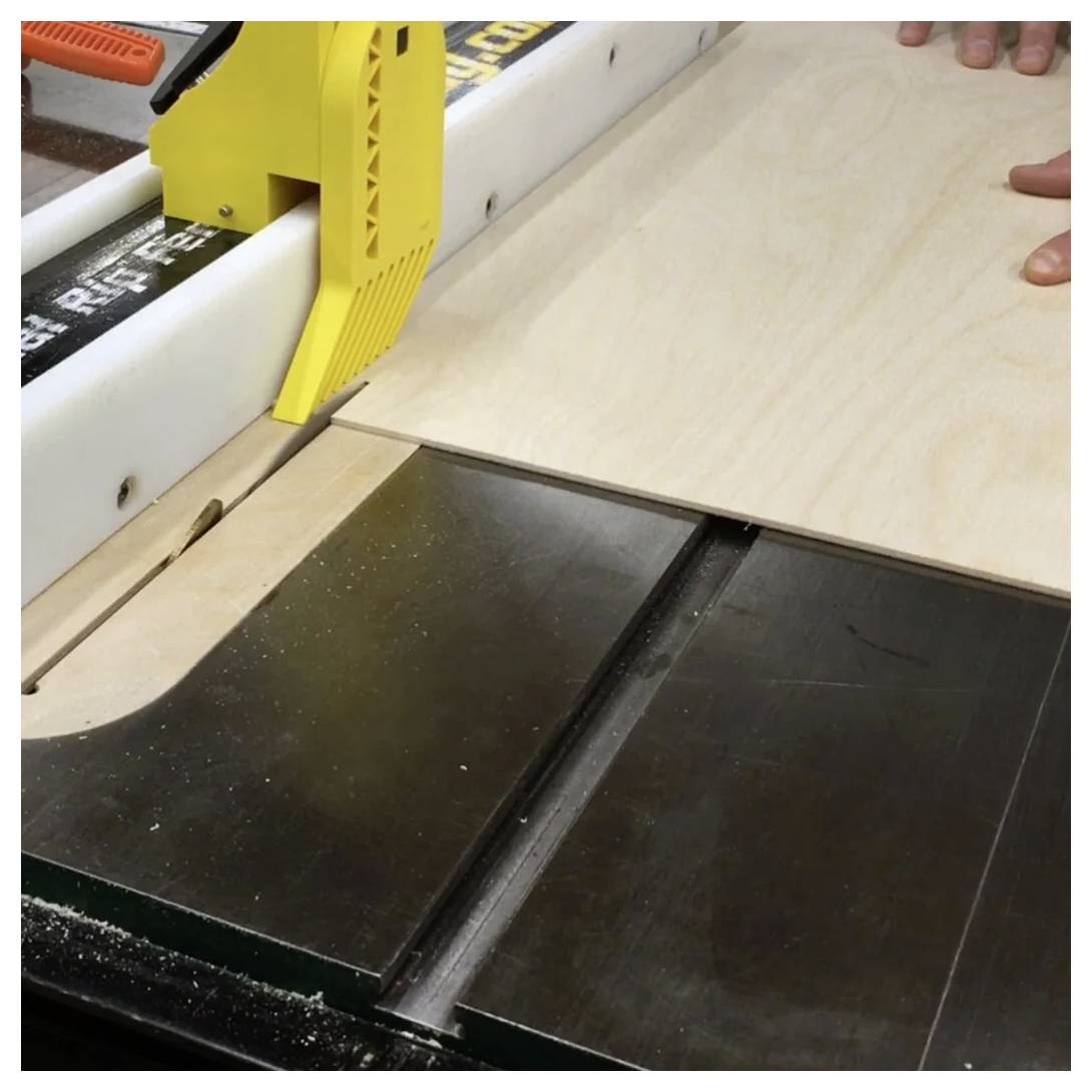 Piła tarczowa tnie drewnianą deskę, prowadzona żółtym popychaczem, a ręce ostrożnie kontrolują ruch deski.