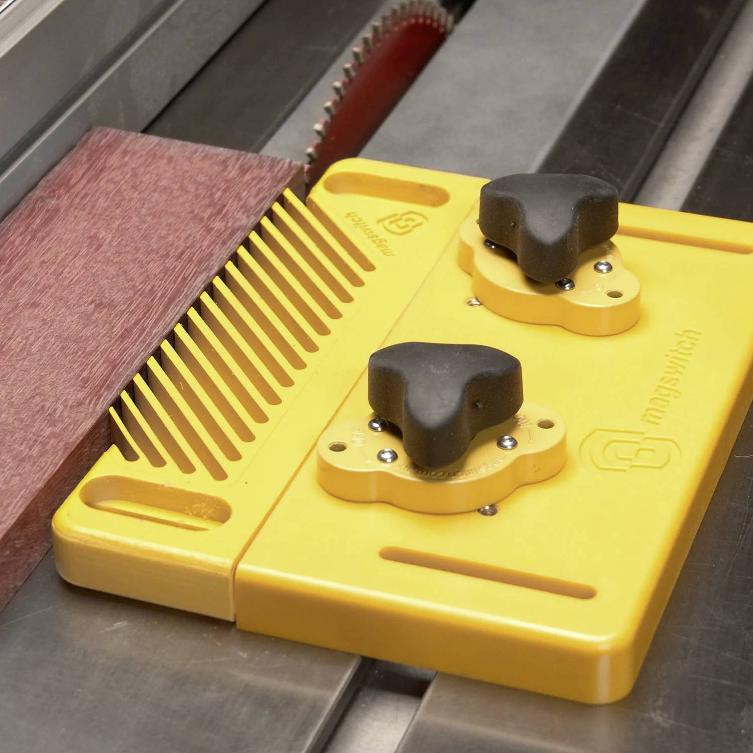 Żółte urządzenie bezpieczeństwa z pokrętłami i grzebykowatą konstrukcją jest zamocowane przy pile tarczowej, prowadząc drewno podczas precyzyjnego i bezpiecznego cięcia.