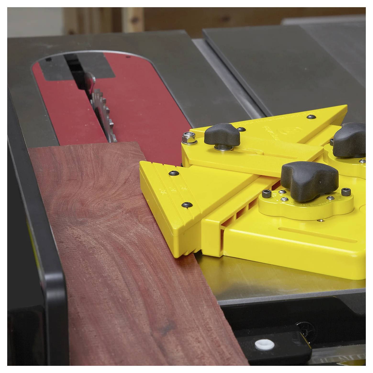 Piła stołowa z żółtym blokiem dociskowym prowadzi kawałek drewna w kierunku ostrza, zapewniając precyzję i bezpieczeństwo podczas cięcia.