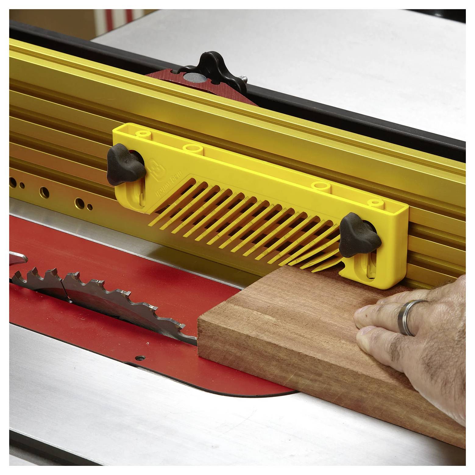 Ręka prowadzi kawałek drewna przez piłę stołową, używając żółtego prowadnika bezpieczeństwa, aby zapewnić precyzję i bezpieczeństwo podczas cięcia.