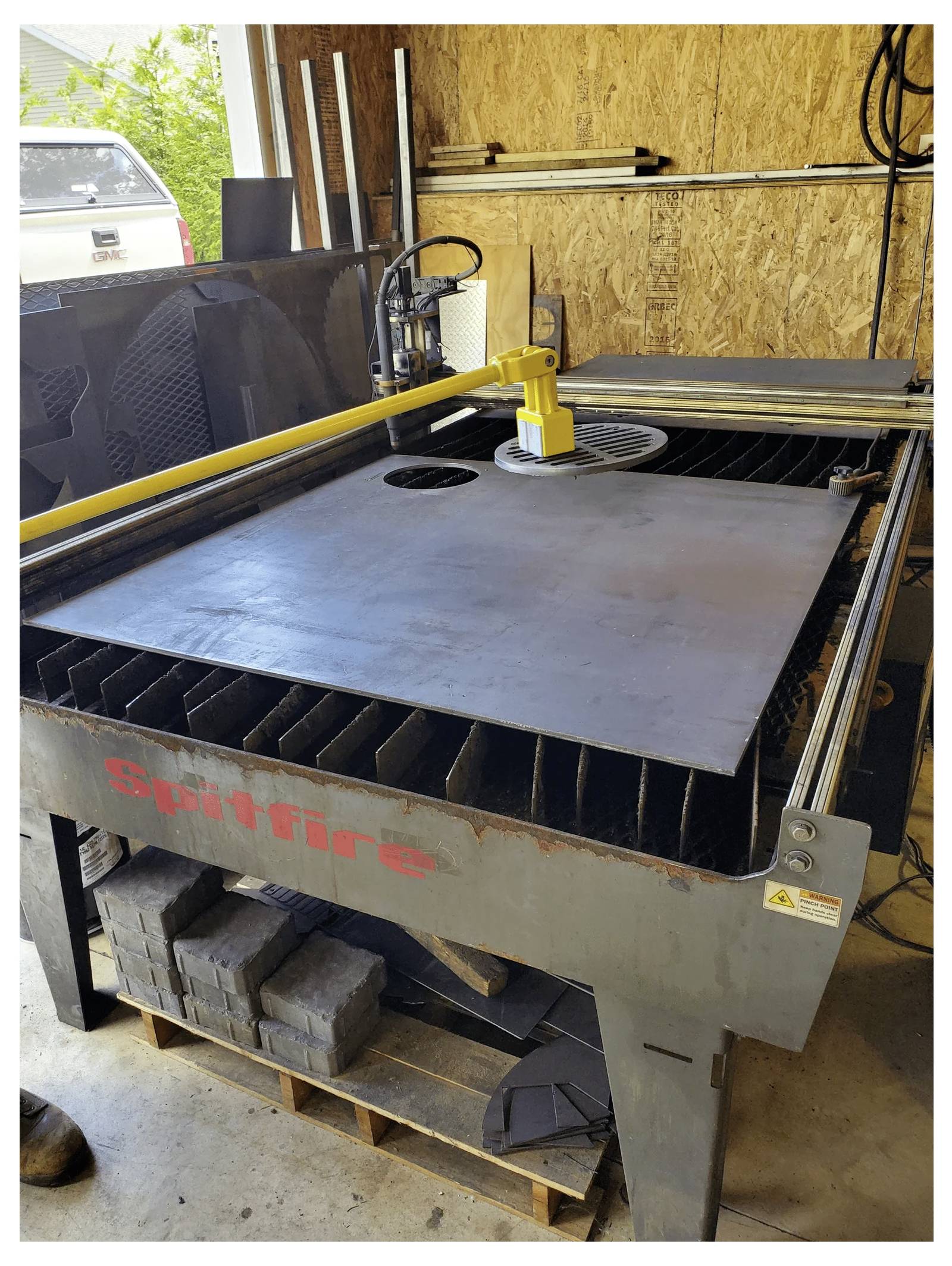 Przemysłowa maszyna tnąca w warsztacie, z dużą metalową płytą ustawianą pod żółtym ramieniem do cięcia, oznaczona etykietą Spitfire.