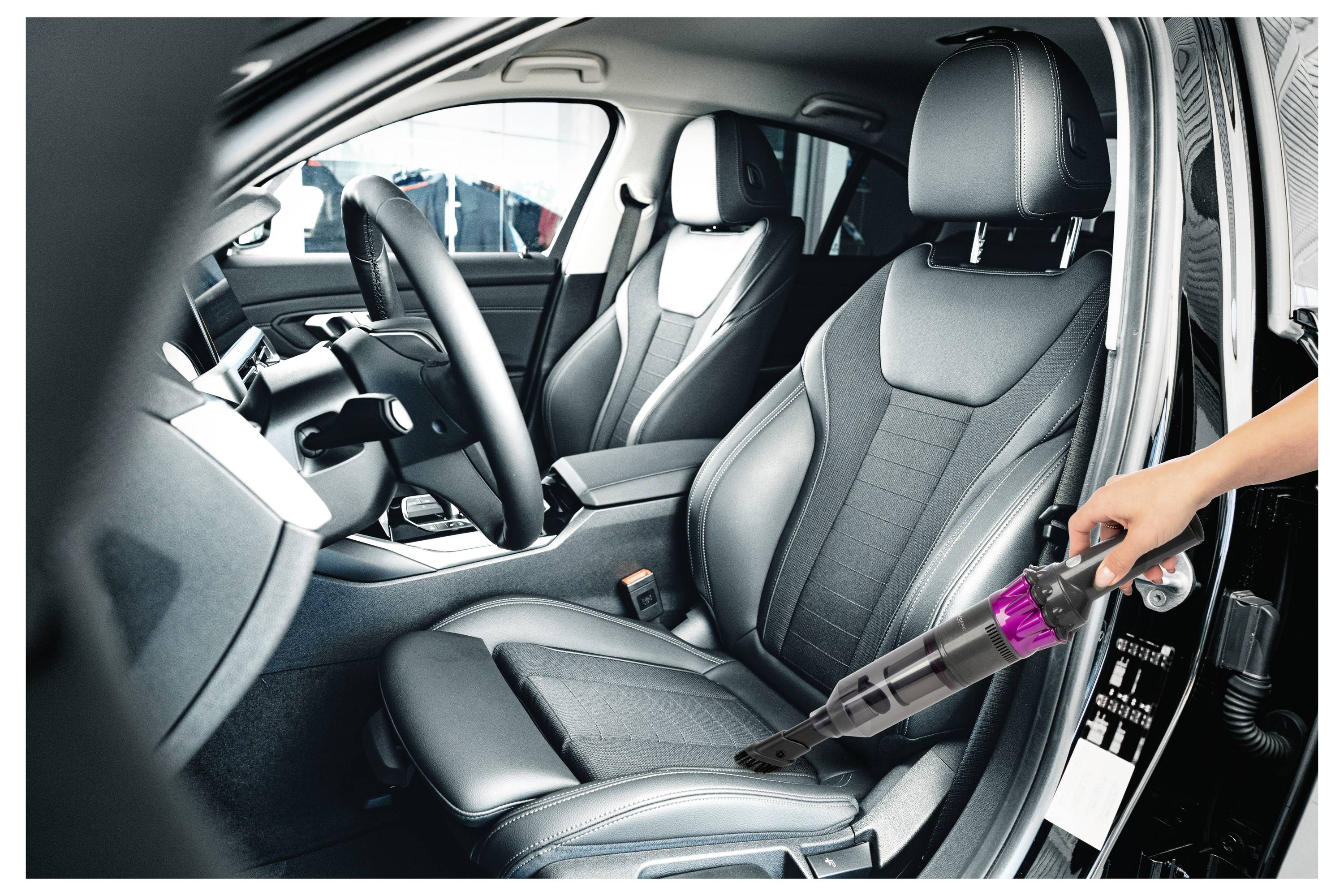 Osoba używa ręcznego odkurzacza do czyszczenia fotela pasażera z przodu samochodu, koncentrując się na siedzeniu i przylegającym obszarze.