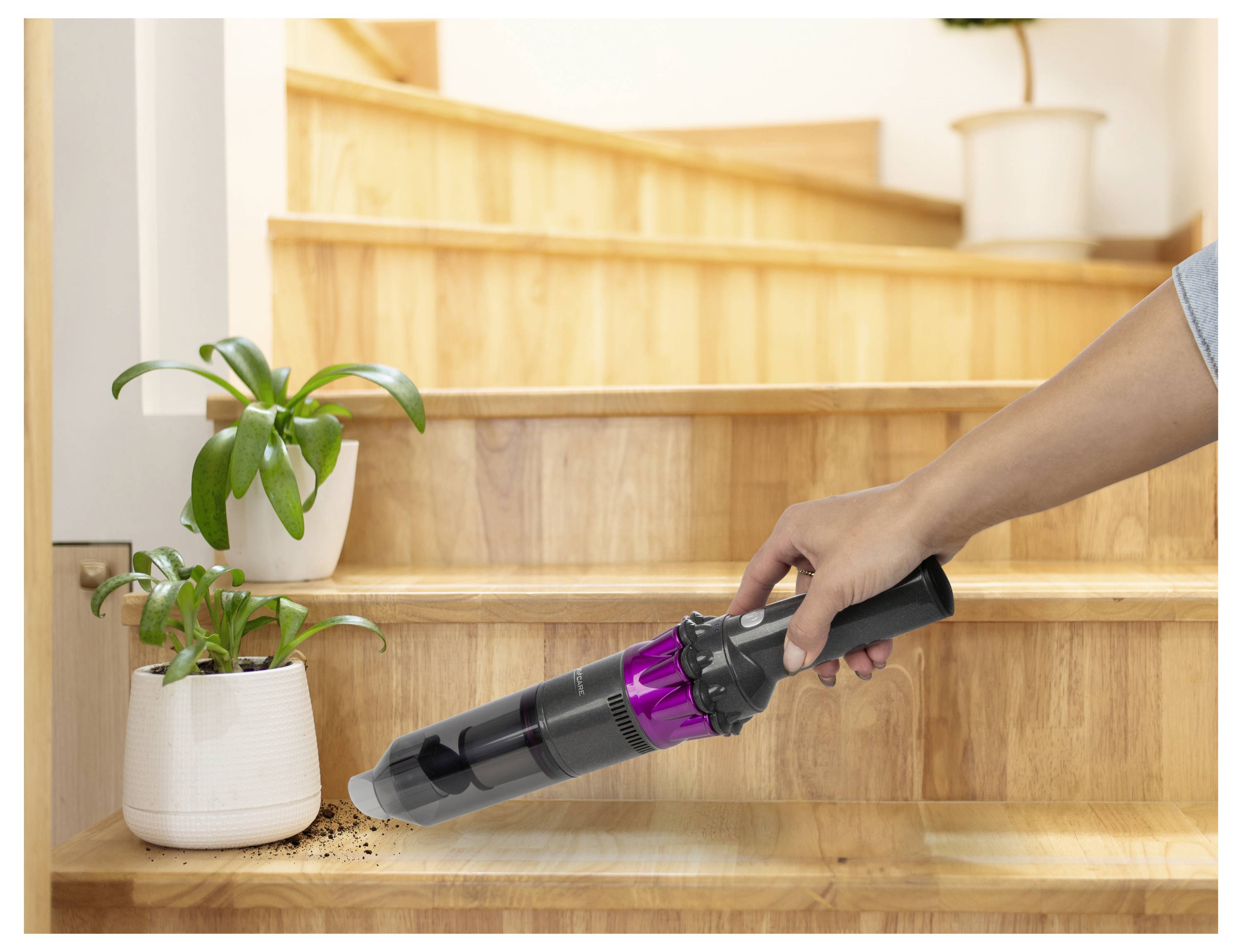 Osoba używa ręcznego odkurzacza do usunięcia brudu rozlanego w pobliżu małej rośliny na drewnianych schodach.