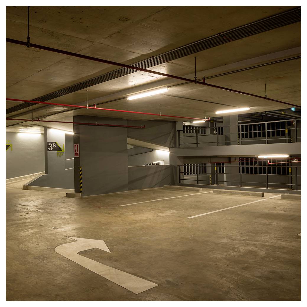 Pusty parking podziemny z wyznaczonymi miejscami postojowymi oraz znakiem '3A' na ścianie. Strzałka kierunkowa na podłodze wskazuje w lewą stronę.