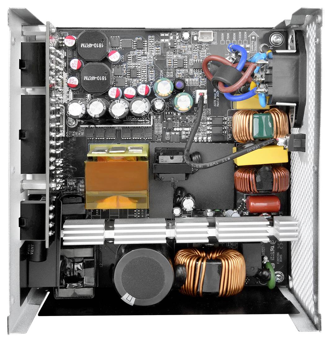 Widok z góry wnętrza jednostki zasilającej komputera, przedstawiający kondensatory, cewki i różne elementy elektroniczne na płytce drukowanej.