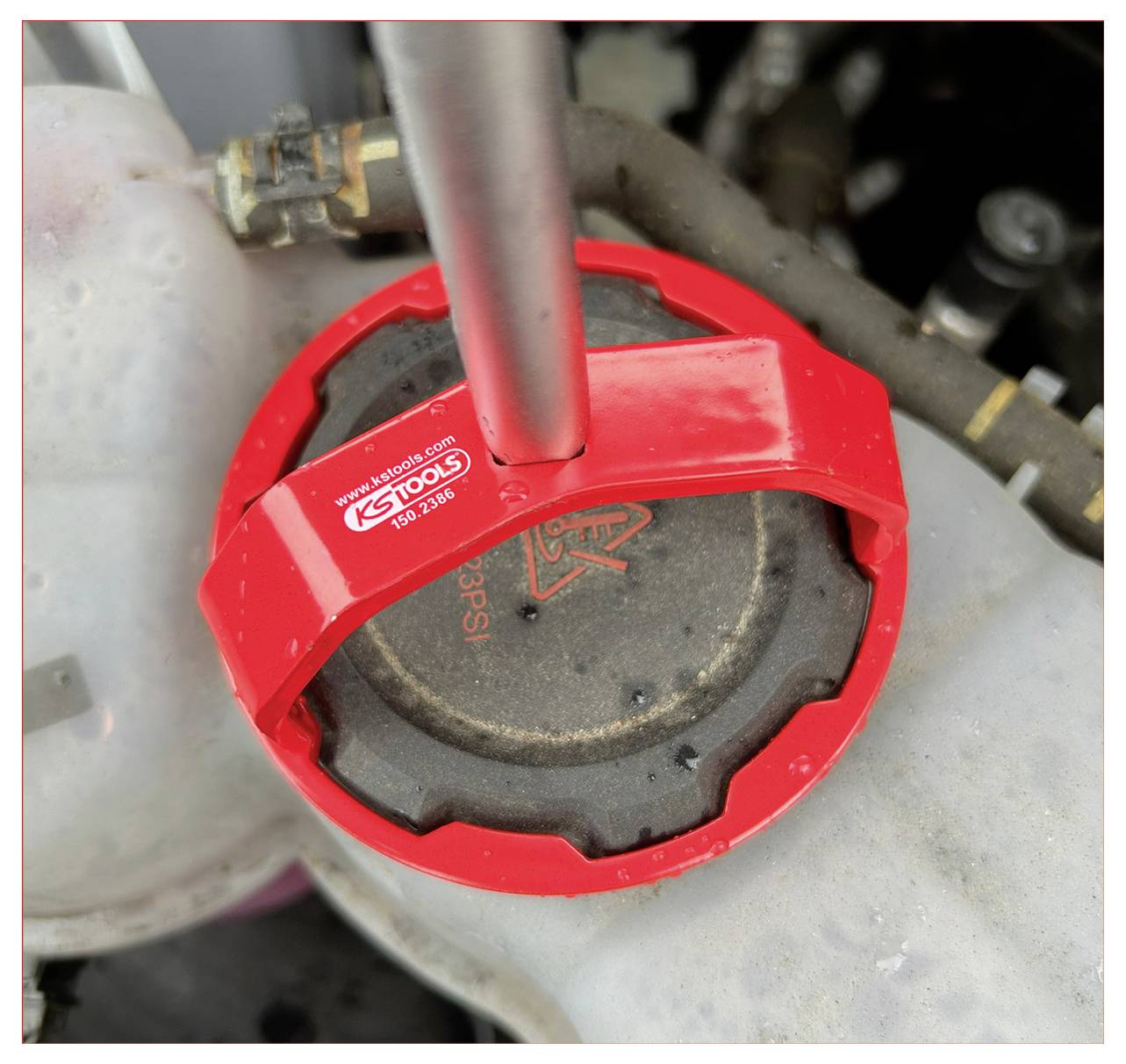 Zbliżenie czerwonego urządzenia marki KS Tools umieszczonego na czarnym elemencie silnika, sugerujące konserwację lub naprawę pojazdu.