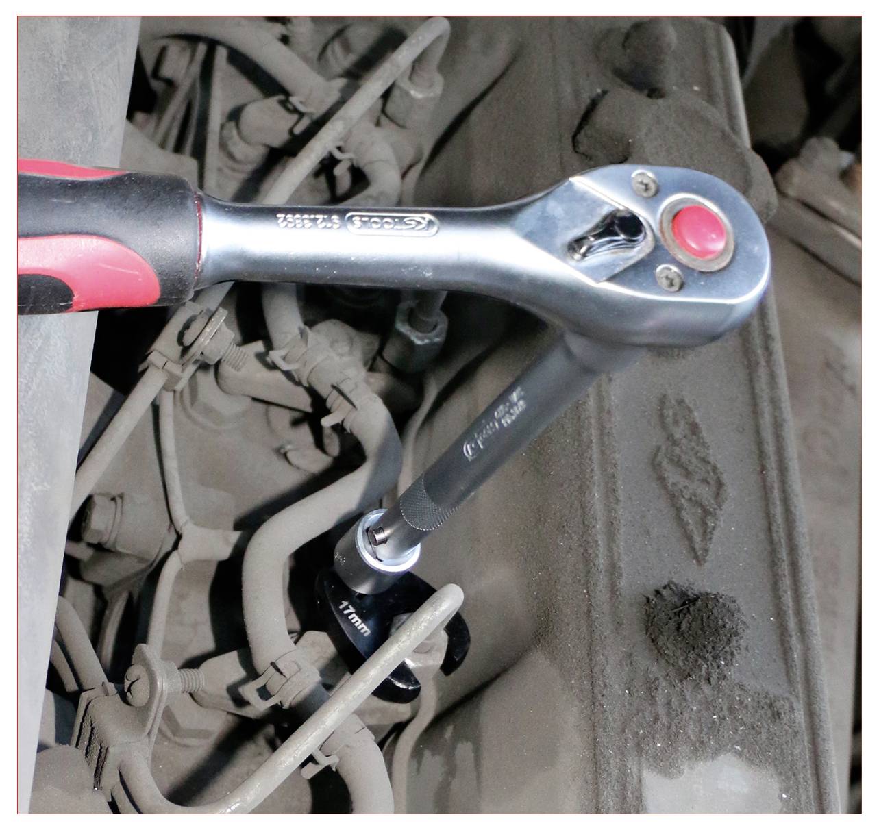 Klucz grzechotkowy zaciska śrubę na zakurzonej części silnika, prezentując zastosowanie narzędzia w naprawie samochodowej.