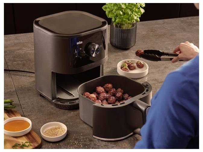 Osoba używa szczypiec do włożenia pulpetów do miski obok frytkownicy powietrznej stojącej na blacie kuchennym, z przyprawami i sosem w pobliżu.