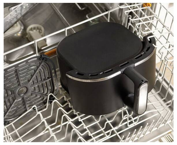 Kosz i tacka z frytownicy powietrznej są umieszczone wewnątrz zmywarki, co wskazuje na to, że są one w trakcie mycia.