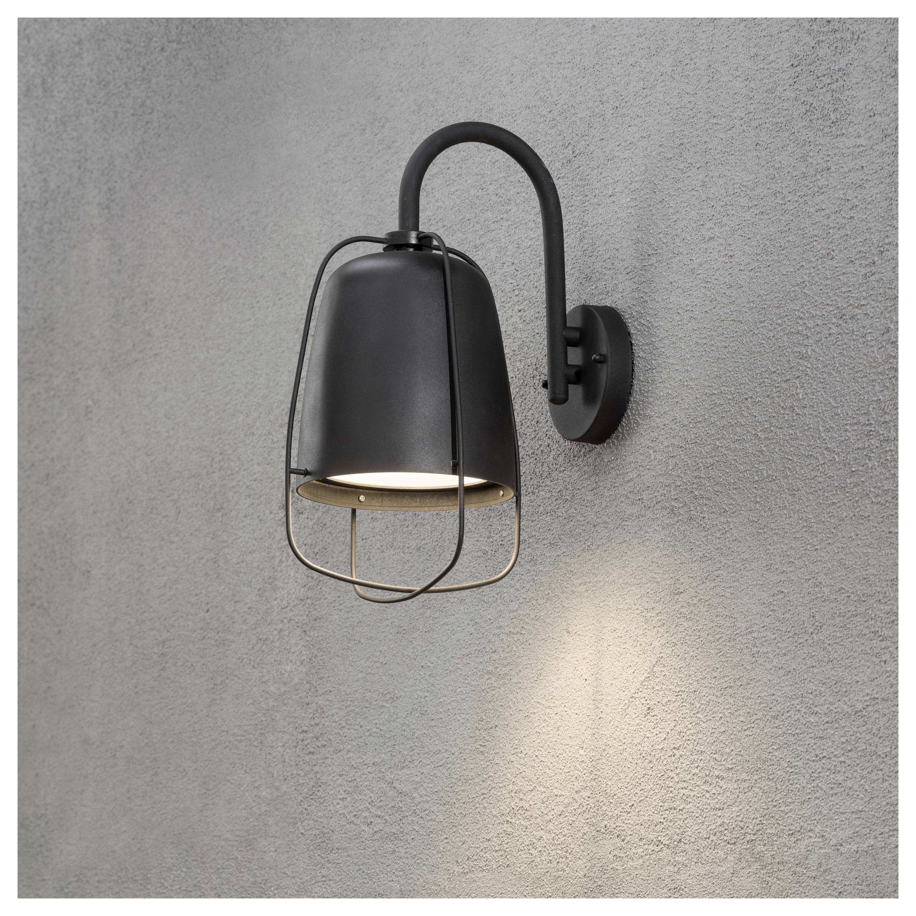 Czarna lampa naścienna w stylu klatki, przeznaczona do użytku na zewnątrz, jest zamontowana na szarej ścianie i rzuca łagodne, skierowane w dół światło.