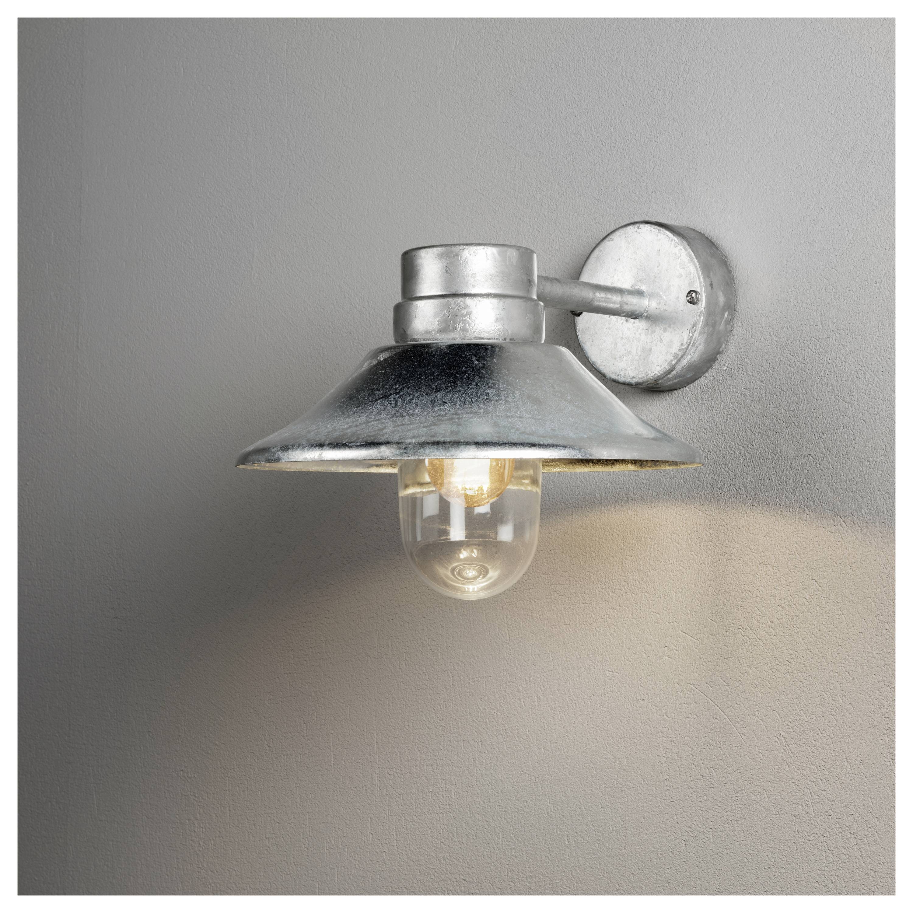Kinkiet w stylu przemysłowym zamocowany na ścianie, wyposażony w szeroki metalowy klosz, oświetlający niewielką sekcję szarej ściany za sobą.
