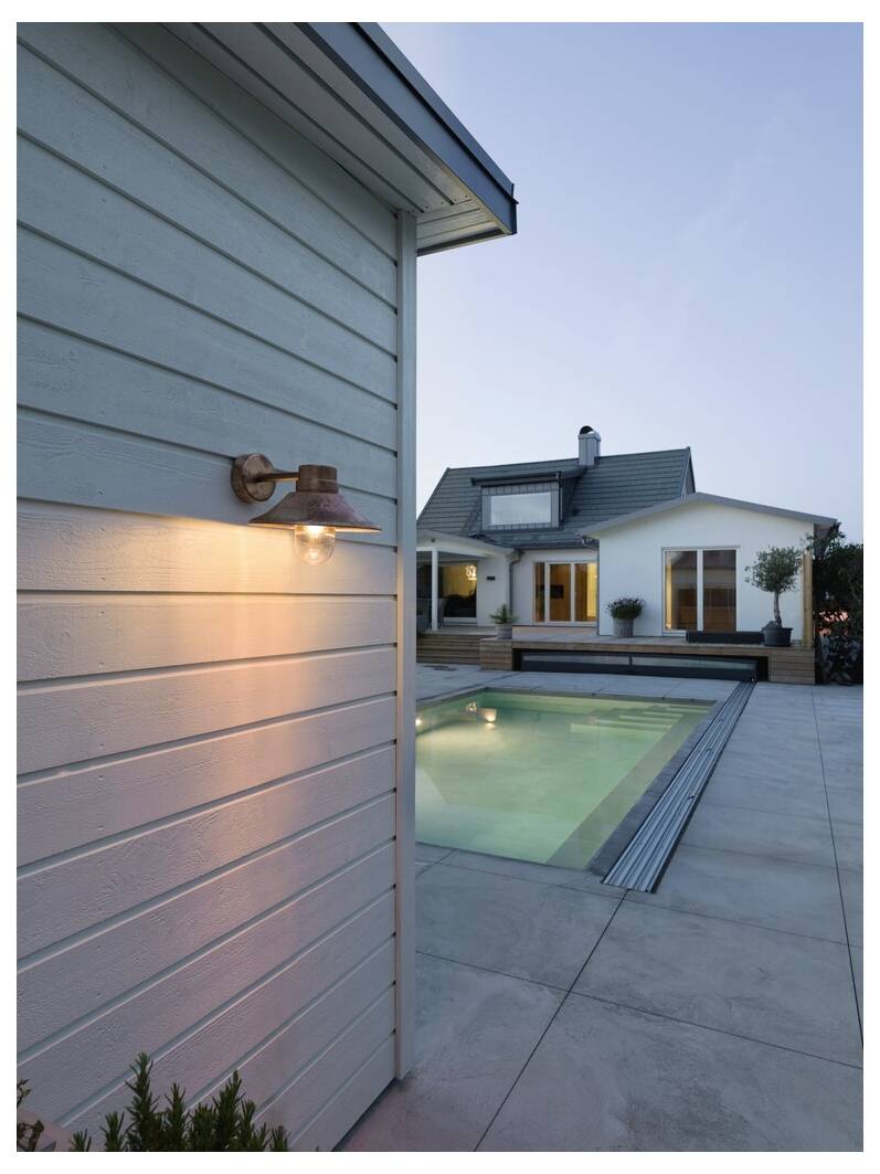 Nowoczesny dom z dużymi oknami widoczny jest o zmierzchu. Na tylnym podwórku znajduje się włączona lampa zewnętrzna przymocowana do elewacji oraz basen pływacki.