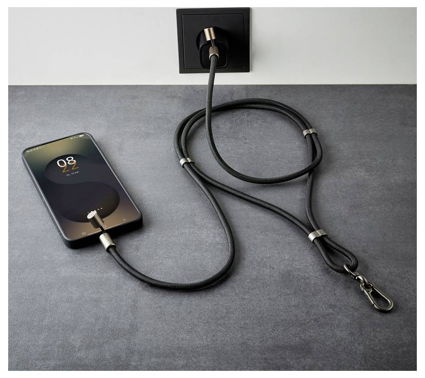 Smartfon wyświetlający '8:22' ładuje się na szarej powierzchni, podłączony czarnym kablem do gniazdka elektrycznego.