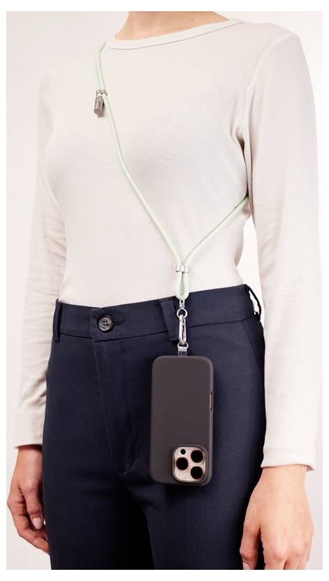 Osoba ubrana w top w neutralnym kolorze i ciemne spodnie, prezentująca smartfon przymocowany do paska przewieszonego przez ramię, umożliwiającego noszenie go bez użycia rąk.