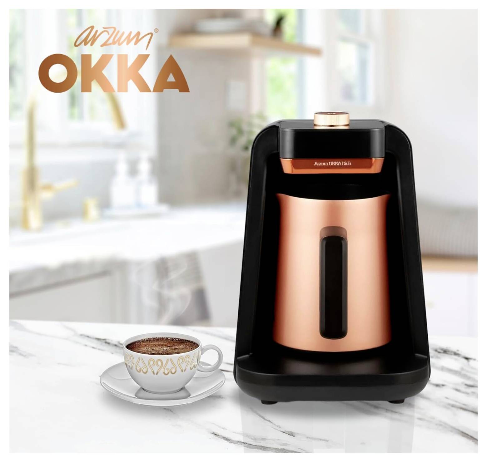 Miedzianokolor ekspres do kawy na marmurowym blacie z filiżanką kawy przed nim. W tle kuchnia z rozmytym zlewem i dekoracjami. Oznaczenie marki 'Arzum OKKA'.