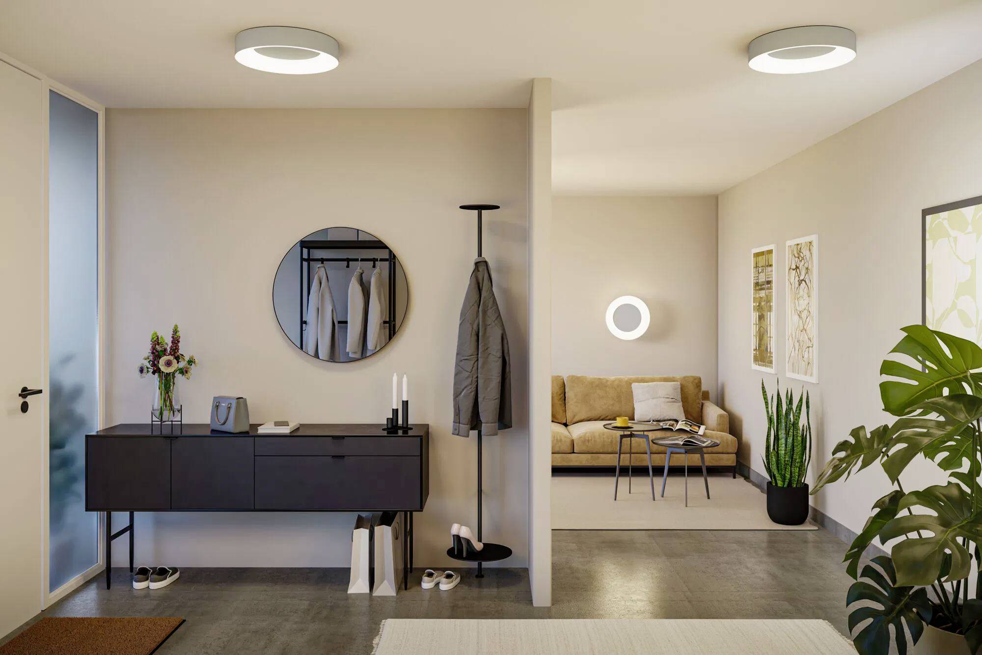 Nowoczesne, minimalistyczne wnętrze z przedpokojem wyposażonym w lustro, wieszak na ubrania i konsolę. Przytulna strefa wypoczynkowa jest widoczna, z kanapą, stolikiem kawowym i doniczkowymi roślinami, tworząc przyjazną atmosferę.