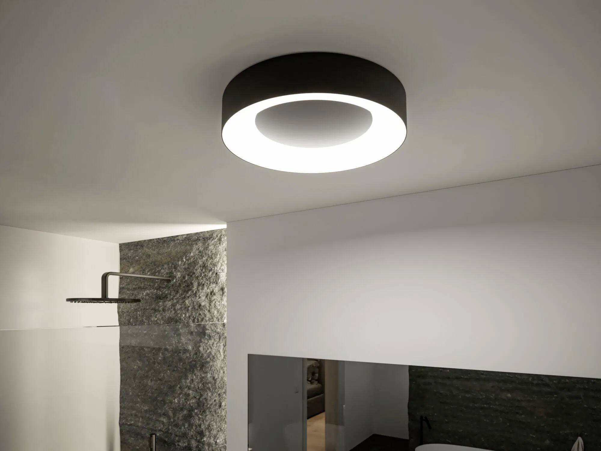 Nowoczesna okrągła lampa sufitowa w minimalistycznym pokoju, oświetlająca teksturowaną ścianę i przeszklony obszar prysznica poniżej.