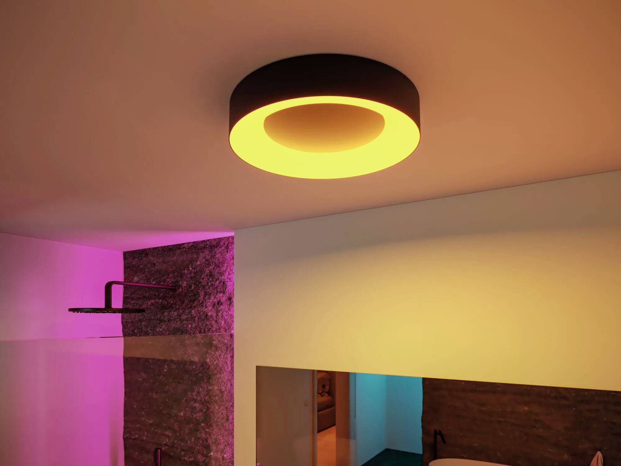 Nowoczesna lampa sufitowa o ciepłym świetle oświetla pomieszczenie z różowymi i niebieskimi akcentami na kamiennych i białych ścianach, tworząc przytulny klimat.