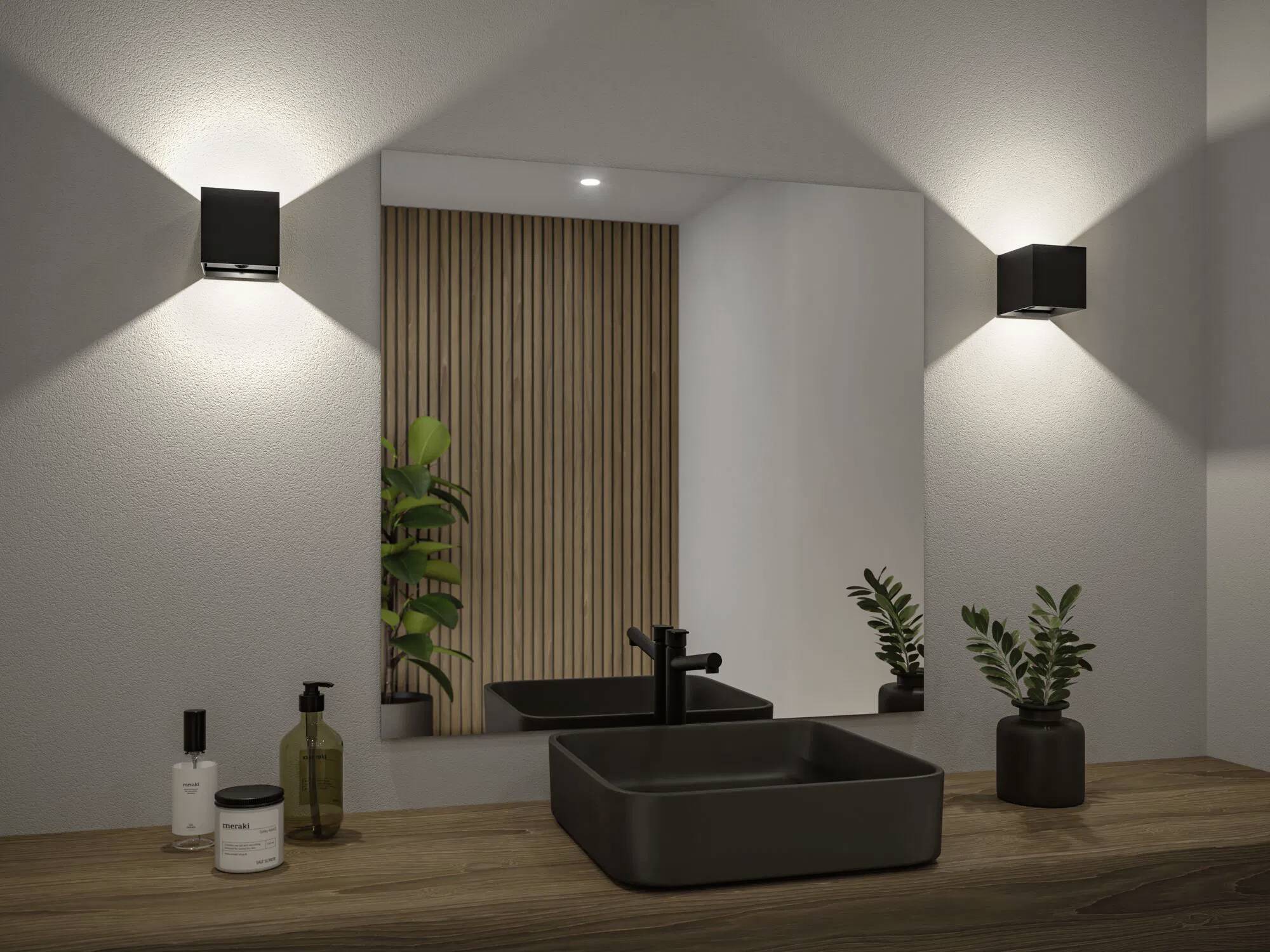 Nowoczesna łazienka prezentuje się ze kwadratową czarną umywalką, baterią i małymi roślinami na drewnianym blacie, pod prostokątnymi kinkietami ściennymi.