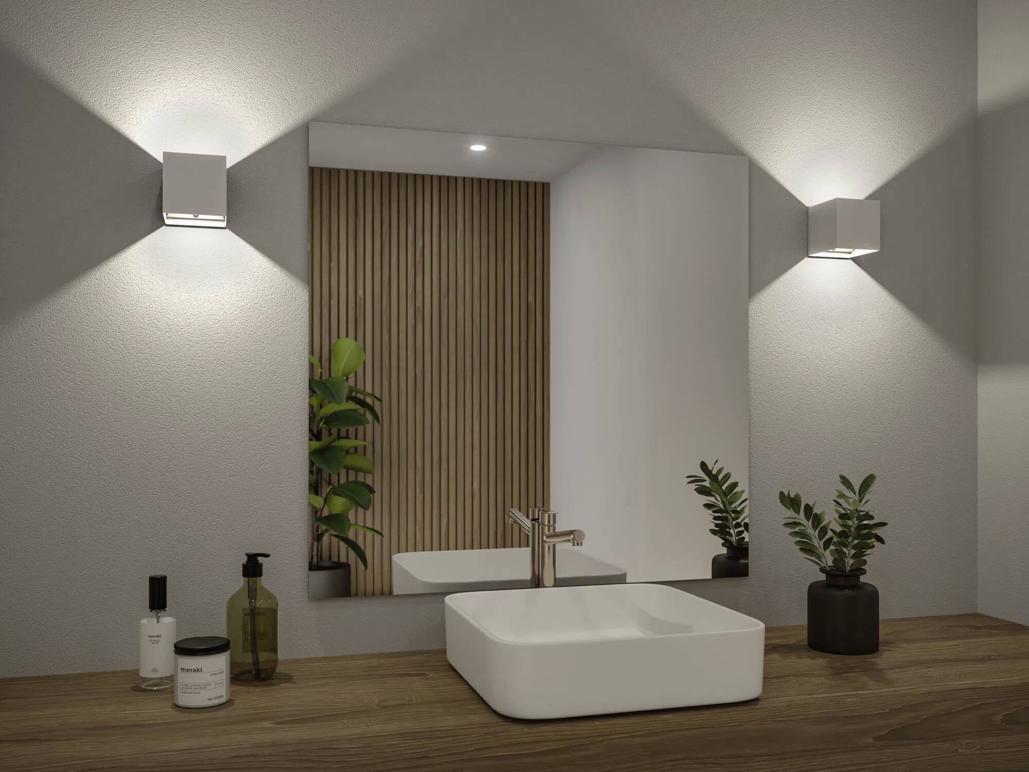 Nowoczesna łazienka z drewnianym blatem, prostokątną białą umywalką, dużym lustrem, roślinami i dwoma kinkietami zapewniającymi miękkie oświetlenie.