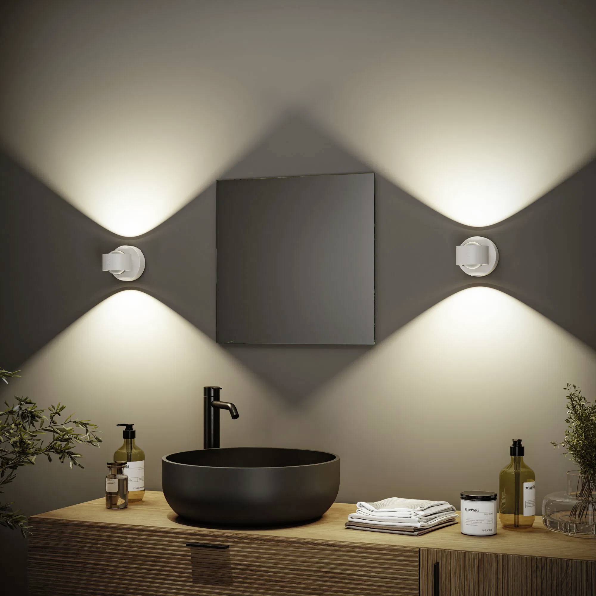 Obszar umywalki łazienkowej z czarną okrągłą miską, nowoczesną baterią, podświetlanym lustrem, przyborami toaletowymi i dekoracyjnymi roślinami.