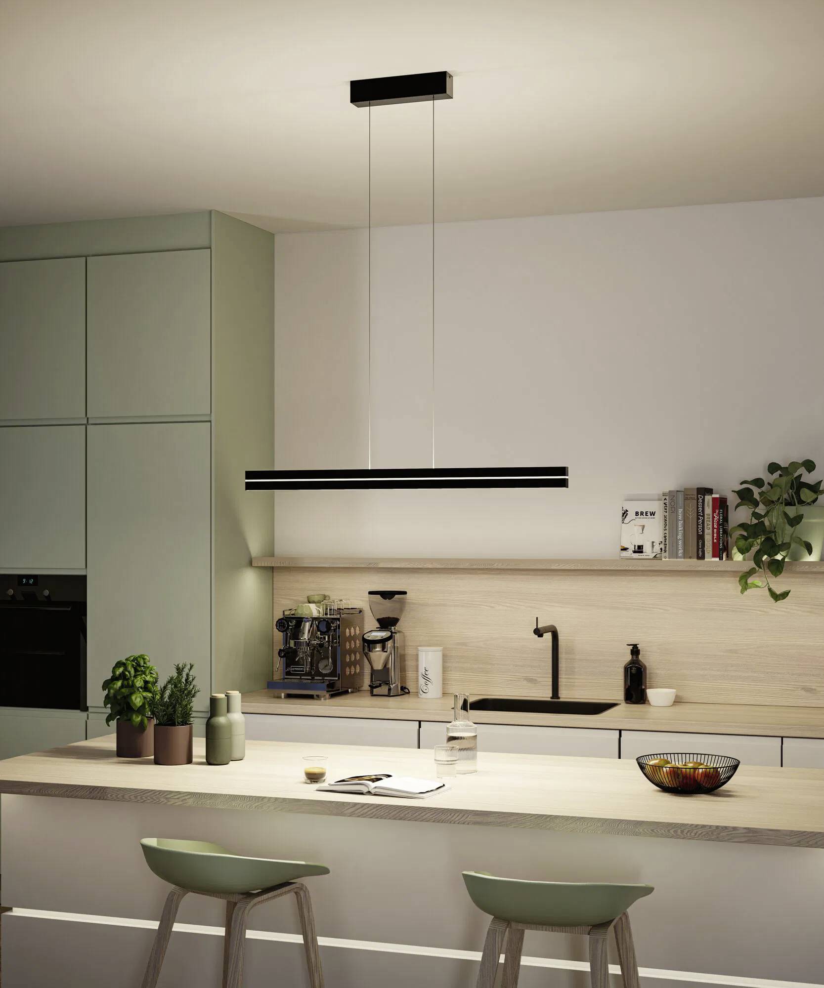 Nowoczesna kuchnia z wiszącą lampą nad wyspą kuchenną, wyposażona w hokery barowe, rośliny oraz ekspres do kawy na jasnodrewnianym blacie.
