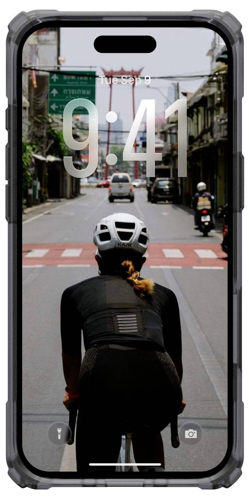 Rowerzysta w kasku jedzie po pustej ulicy z tablicami informacyjnymi nad głową. Widoczny jest interfejs telefonu, na którym wyświetlana jest godzina '9:41'.