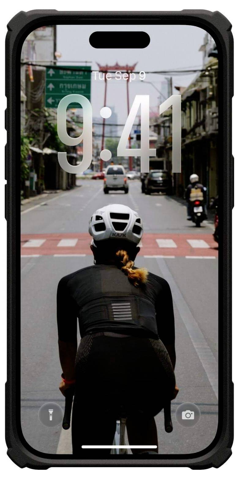 Ekran smartfona pokazuje rowerzystę na ulicy miejskiej, ubranego w kask i czarny strój, jadącego w kierunku przejścia dla pieszych, z godziną '9:41'.