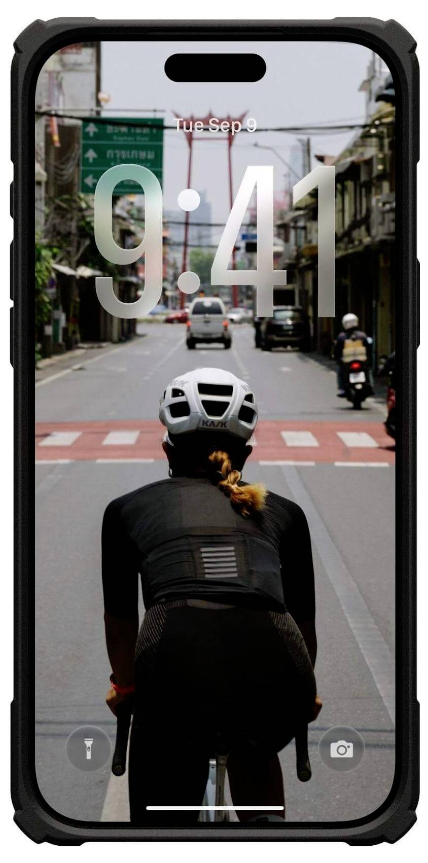 Na smartfonie wyświetla się ekran blokady przedstawiający rowerzystę jadącego po pustej ulicy, z czasem '9:41' nałożonym na obraz.