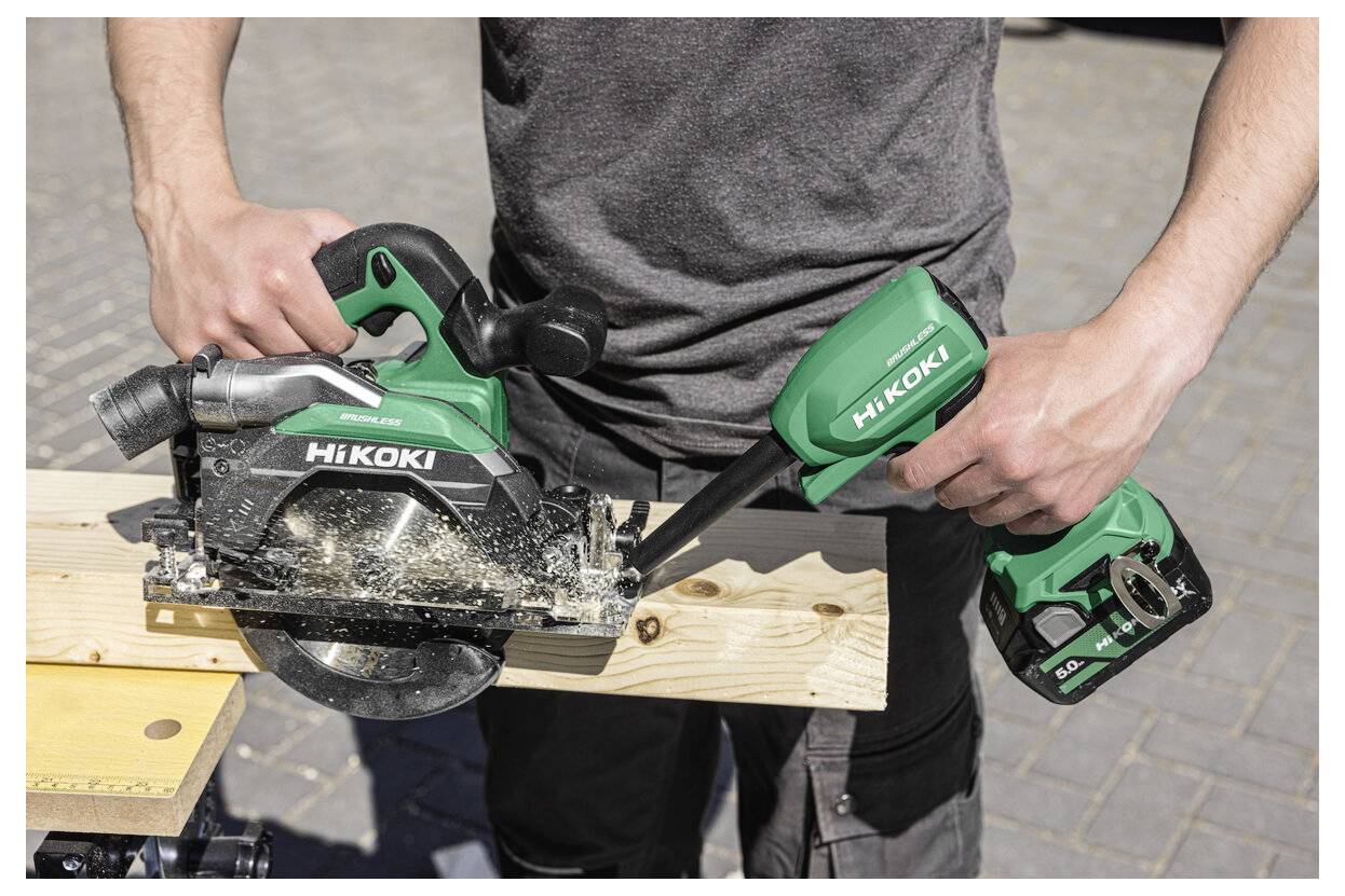 Osoba używająca zielonej piły tarczowej HiKOKI do cięcia drewnianej deski na stole warsztatowym. Widoczne są wióry, co wskazuje na aktywne użycie narzędzia.