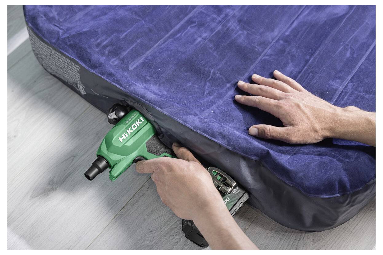Osoba pompuje niebieską materac powietrzną za pomocą zielonego narzędzia marki HiKOKI, trzymając rękę na materacu dla zachowania stabilności.