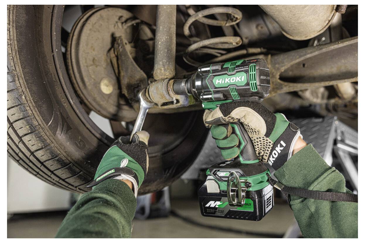 Osoba w zielonych rękawicach używa zielonego elektronarzędzia do pracy przy zawieszeniu samochodu, koncentrując się na komponencie koła.