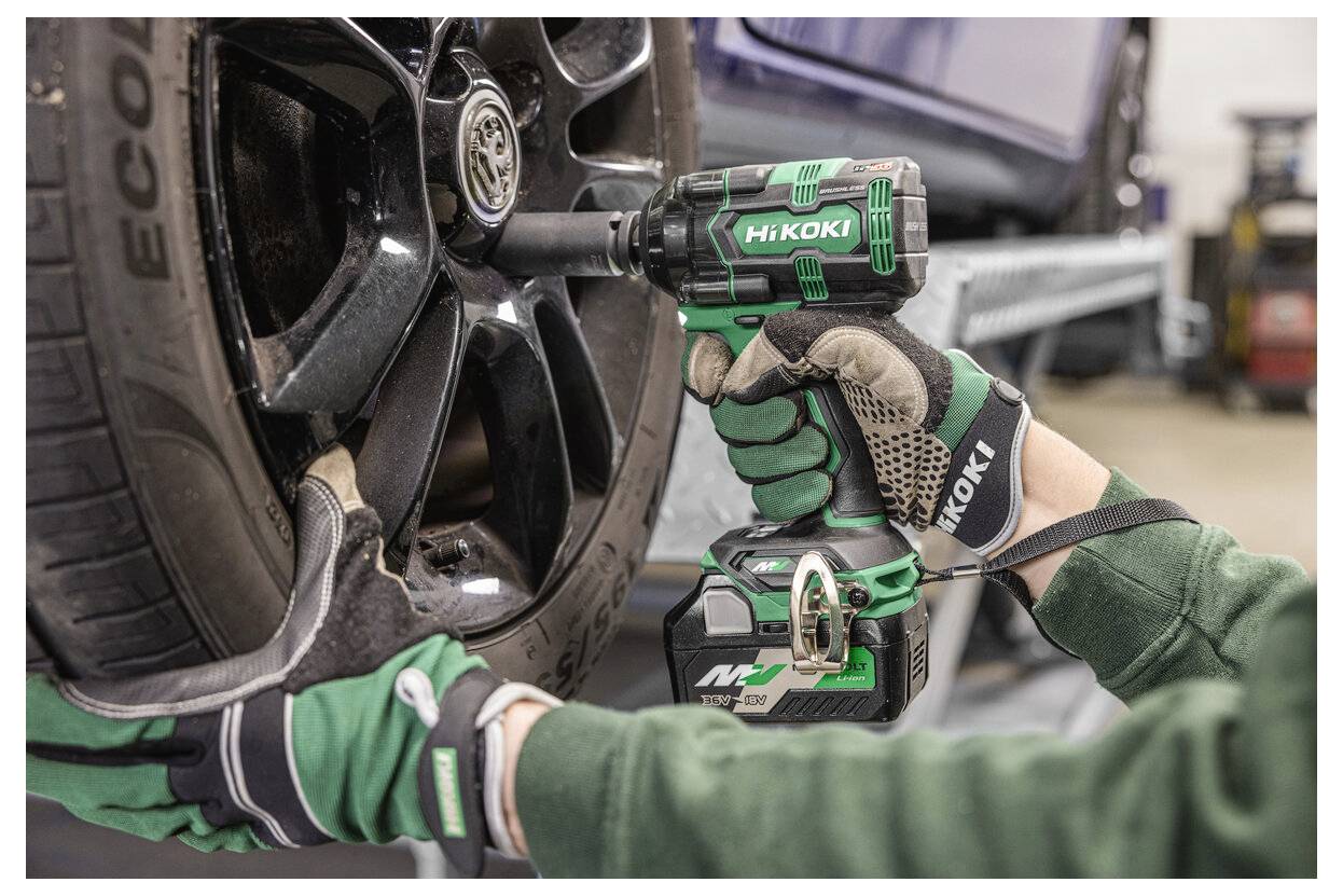 Osoba w rękawicach roboczych używa akumulatorowego klucza udarowego do dokręcenia nakrętki koła samochodu w warsztacie samochodowym.