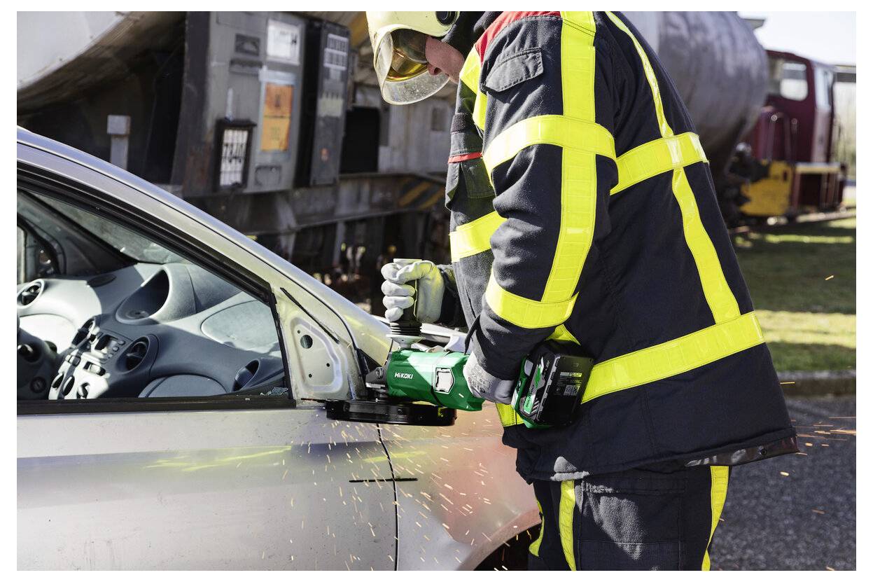Strażak w pełnym sprzęcie ochronnym używa potężnego narzędzia do przecięcia drzwi samochodu podczas akcji ratunkowej, a wokół tryskają iskry.